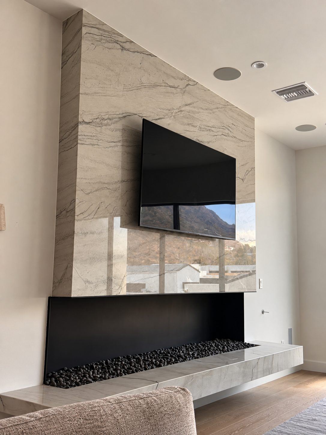 Living room wall clad in light veined stone above a linear fireplace, with a floating stone hearth and a mounted TV