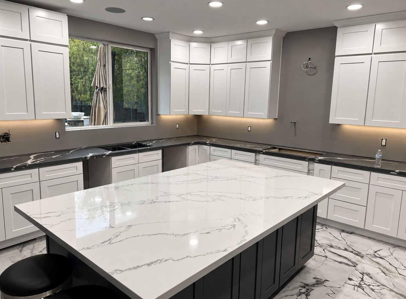 Kitchen with white cabinets, dark veined perimeter counters, and a large white island with gray veining
